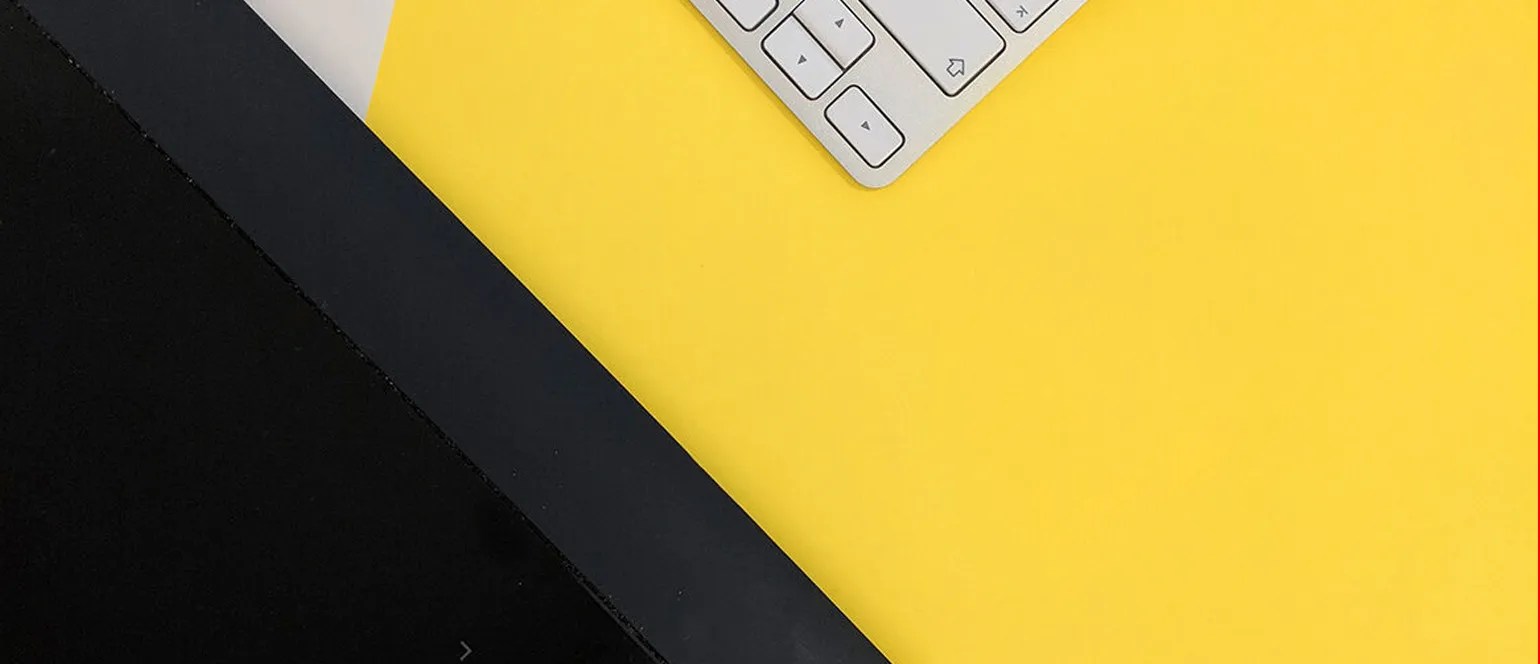 A yellow desk at an angle with the edge of a silver keyboard in the corner